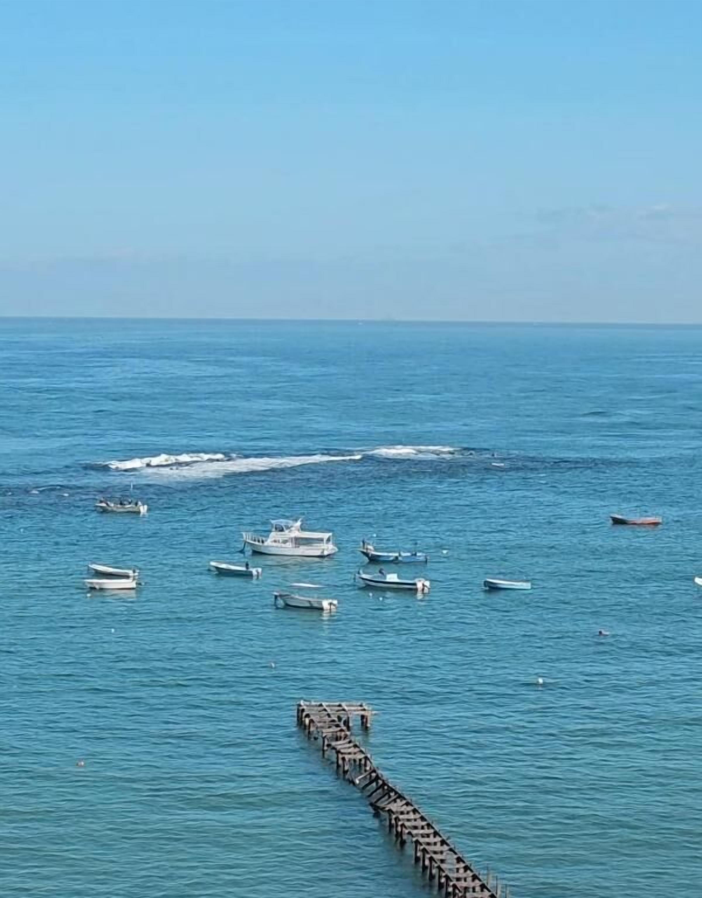 A coastal scene with boats and a pier extending into the water.