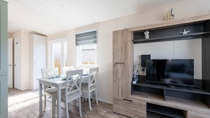 Una cocina moderna con armarios blancos, una mesa de comedor con sillas, un televisor empotrado y una ventana con persianas.