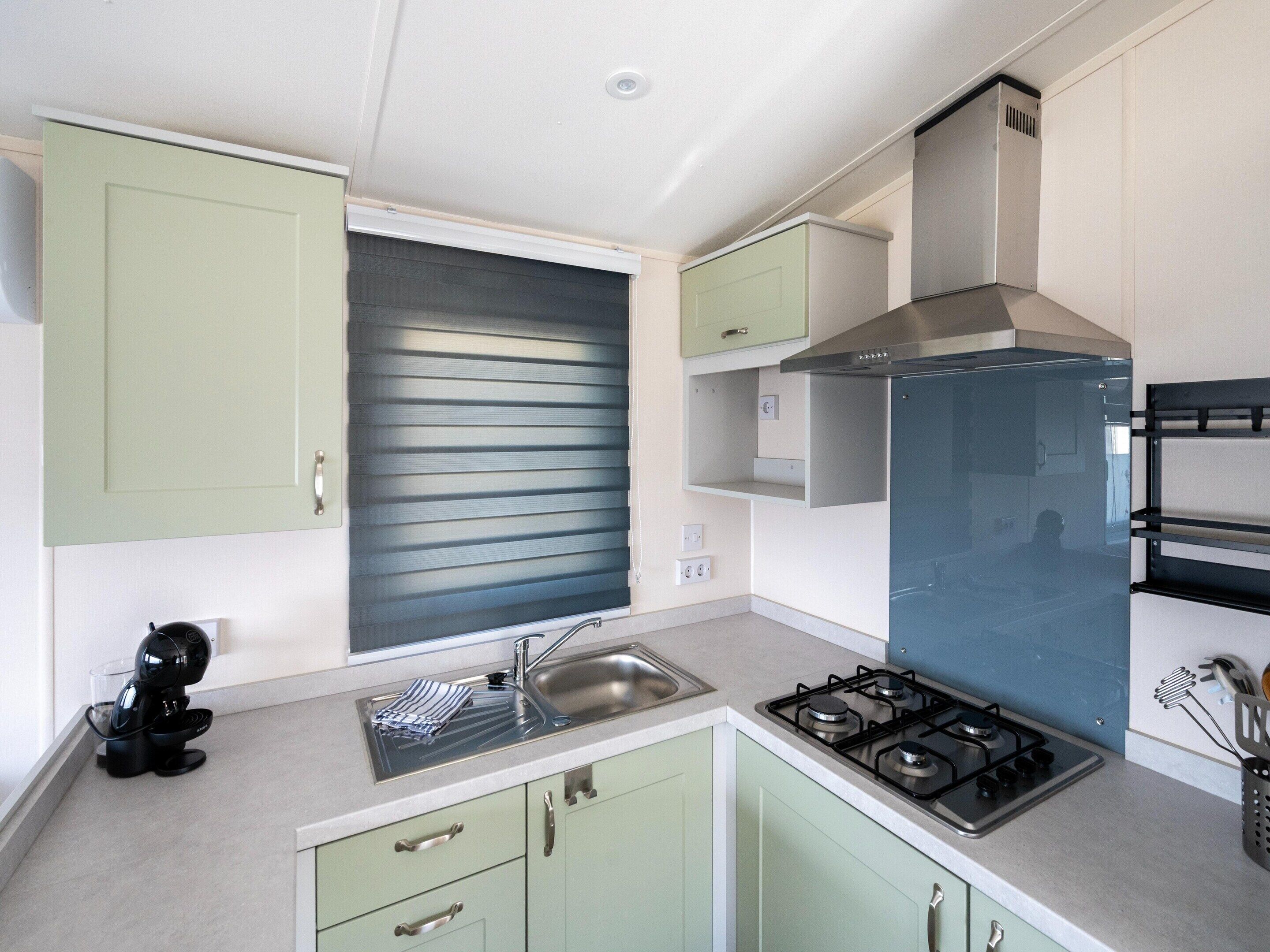 A compact kitchen with a gas stove, a sink, and light green cabinets.