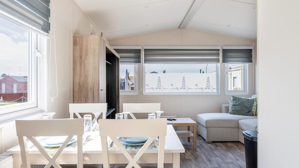 Un comedor con mesa y sillas, un sofá, y vistas a la playa a través de amplias ventanas.