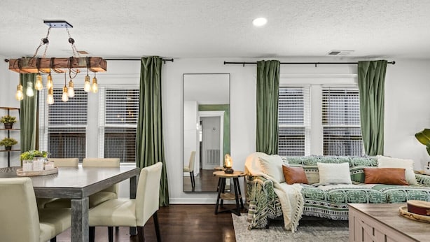 A modern living room with a dining area, green curtains, a sofa, and a chandelier. - Nebula Ranch: 3BR Space Cowboy Retreat, Fire Pit + Mural (Houston)