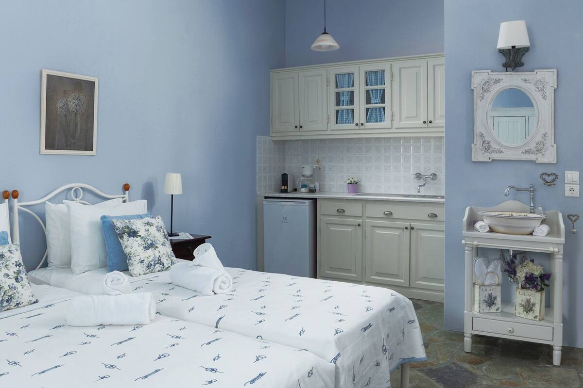 A bedroom with a bed, bedside table, lamp, and a view of the kitchen area.