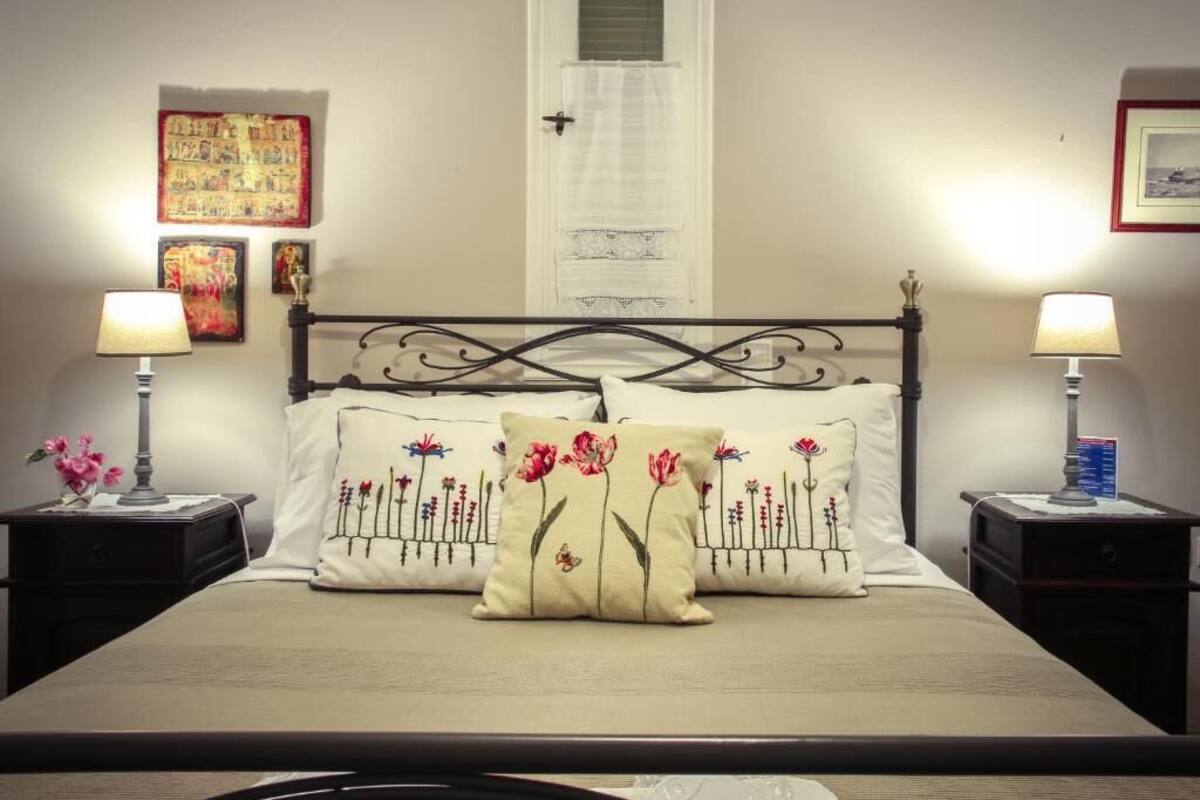 A bed with floral pillows, two bedside lamps, a nightstand with a lamp, and artwork on the walls.