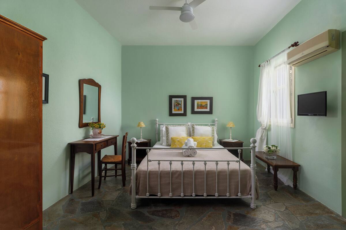 A bedroom with a bed, a desk, a chair, a mirror, and a television.