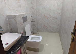 A bathroom with a toilet, sink, and marble walls. - Hotel Four Star (Agra)