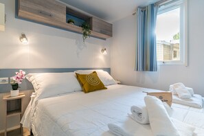 A neatly made bed with white bedding, a single mustard-colored pillow, and a small bedside table with a potted plant. - Vigna Sul Mar Family Collection (Comacchio)