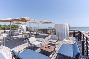 A wooden deck with outdoor seating, umbrellas, and a view of the sea. - Vigna Sul Mar Family Collection (Comacchio)
