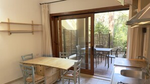 A compact kitchen with a dining area, a sliding glass door leading to an outdoor patio, and a gas stove. - Residence Abbaechelu Santa Margherita (Pula)