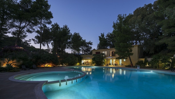 A swimming pool with a curved edge, surrounded by trees and a building with a lighted entrance. - Residence Abbaechelu Santa Margherita (Pula)