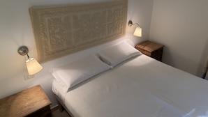 A neatly made bed with white linens, two bedside lamps, a wooden nightstand, and a decorative headboard. - Residence Abbaechelu Santa Margherita (Pula)