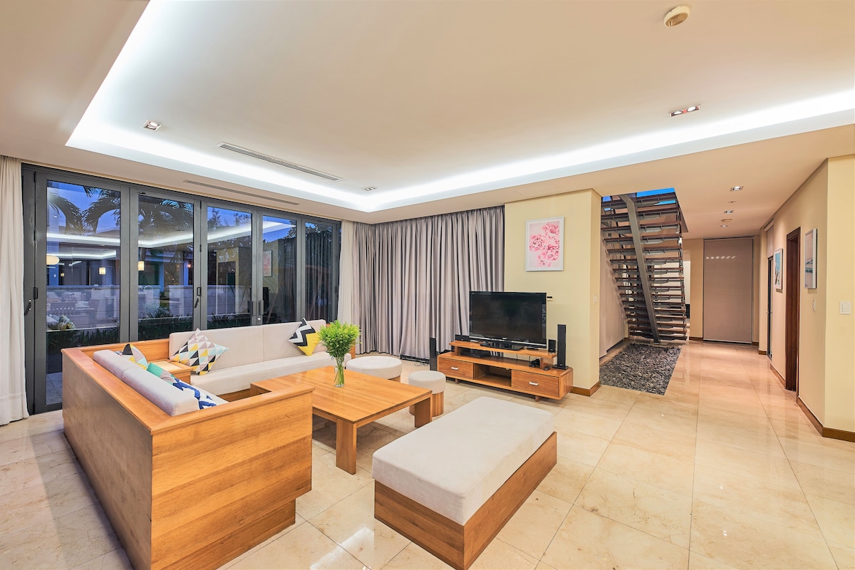 A modern living room with a sofa, coffee table, and TV stand. There is a staircase leading to another level.