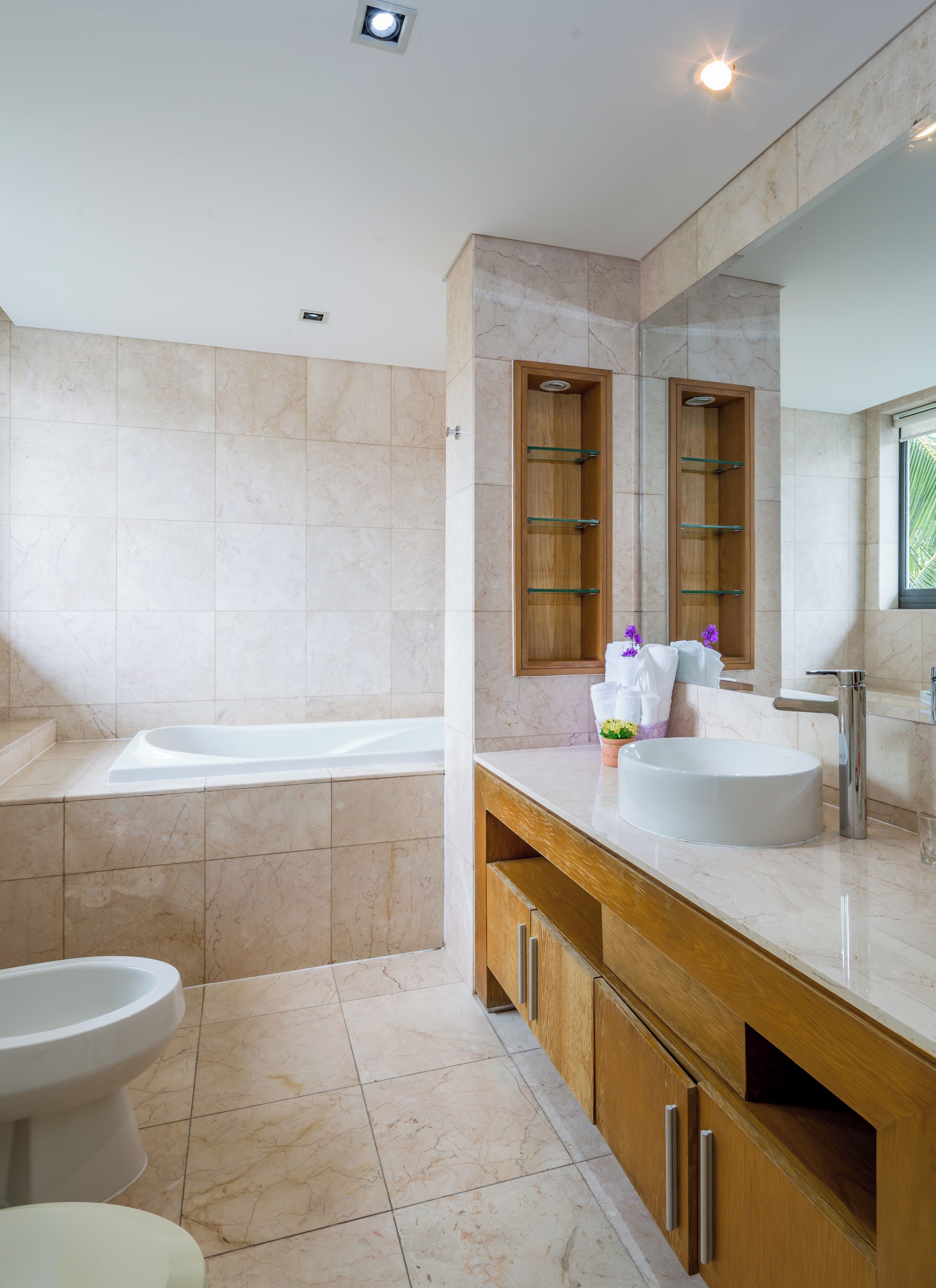 Un baño moderno con una bañera, un lavabo y un inodoro. Se observa un mueble de tocador de madera con un espejo sobre el lavabo.