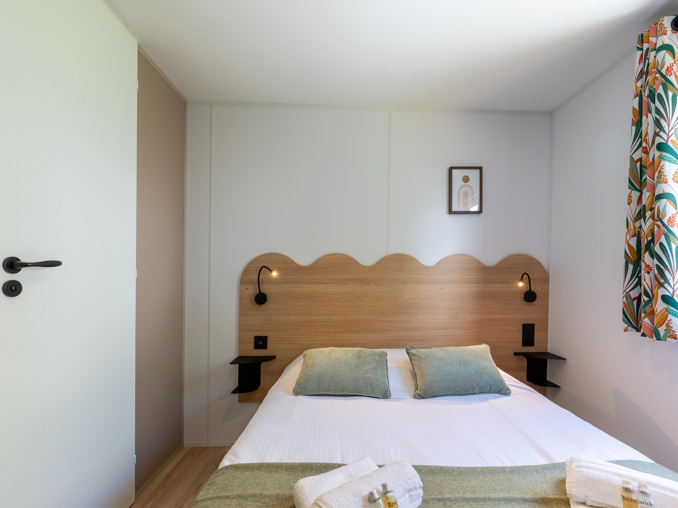 Un letto ben rifatto con una testiera in legno, due comodini e una lampada a parete.