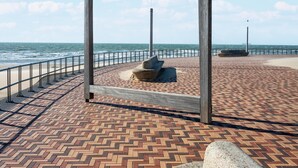 Un paseo marítimo con un sendero de ladrillos estampados, baranda metálica y una estructura de madera.