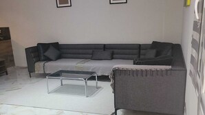 Un salon avec un canapé gris, une table basse en verre et un sol à motifs.