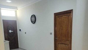 Un couloir avec une porte en bois, une horloge et un banc en marbre.