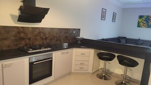 Une cuisine moderne équipée d’une cuisinière à gaz, d’un four, de meubles blancs, de plans de travail noirs et d’un coin bar avec deux tabourets.