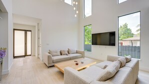 A spacious living room with a large sofa set, a coffee table, and a flat-screen TV mounted on the wall.