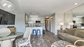 A modern kitchen with white cabinets, a central island, and a dining area with wicker chairs. - Water-View Patio! Condo 2 Mi to Surfside Beach (Myrtle Beach)