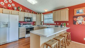 A kitchen with wooden cabinets, a central island with stools, a refrigerator, and a microwave. - 1 Mi to Alto Lake! All-Season Base w/ Mtn Views (Alto)