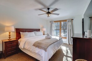 A neatly made bed with a ceiling fan, a bedside lamp, a wooden nightstand, and a window with curtains. - Near Slopes, Trails & Fun! Camelback Townhome (Tannersville)