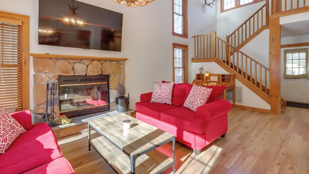 Un salon spacieux avec une cheminée en pierre, un canapé rouge, une table basse en bois et un escalier.