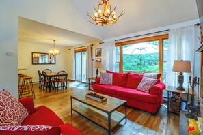 A living room with a red sofa, a coffee table, and a chandelier. There is a dining area with chairs and a table. - Near Slopes, Trails & Fun! Camelback Townhome (Tannersville)