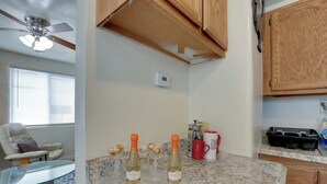 Een keuken met granieten aanrechtbladen, houten kastjes, een plafondventilator en een raam met zonwering.