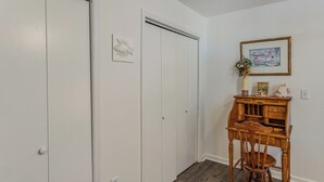 Ein Zimmer mit weißen Wänden, einem Holztisch mit Schubladen, einem Stuhl und einem gerahmten Bild an der Wand.