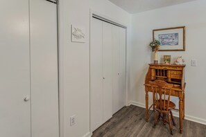 Une pièce aux murs blancs, un bureau en bois avec des tiroirs, une chaise et un tableau encadré accroché au mur.