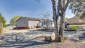 A single-story building with a garage, a gravel driveway, and a tree in the foreground. - Nina's Beach Retreat: ~ 1 Mi to Holden Beach! (Supply)