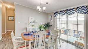 A dining area with a wooden table, white chairs, and a chandelier. - Nina's Beach Retreat: ~ 1 Mi to Holden Beach! (Supply)