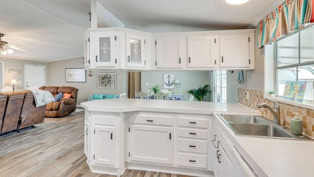 A kitchen with white cabinets, a large island, and a dining area with a brown leather couch. - Nina's Beach Retreat: ~ 1 Mi to Holden Beach! (Supply)