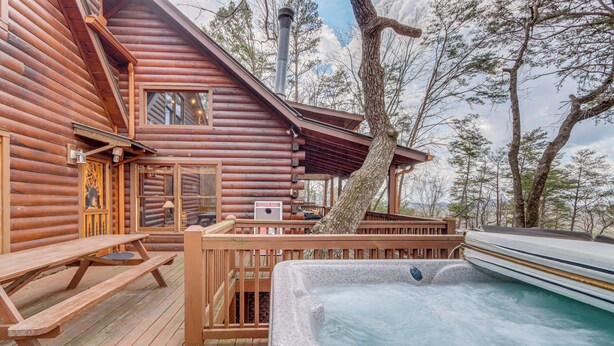 Eine Blockhütte mit Whirlpool, Holzterrasse und Picknicktischen.
