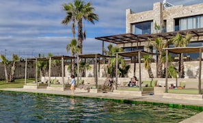 A poolside area with outdoor seating, palm trees, and a stone building in the background. - Zayyna (Ghazoua)