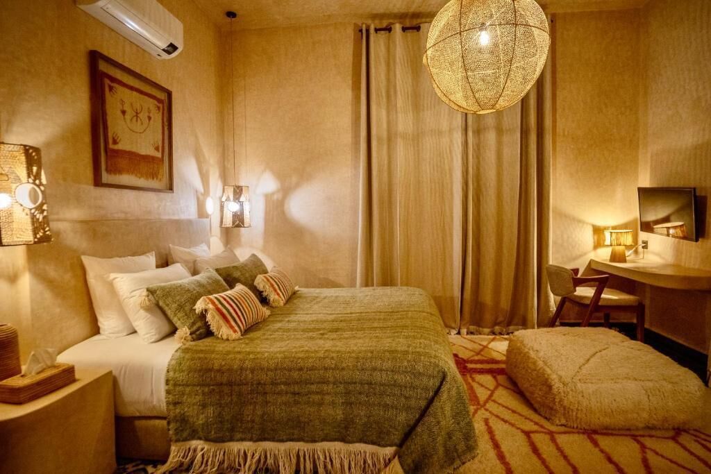 Une chambre d’hôtel comprenant un lit, une table de chevet, une lampe, une chaise et un grand luminaire en matière tressée.
