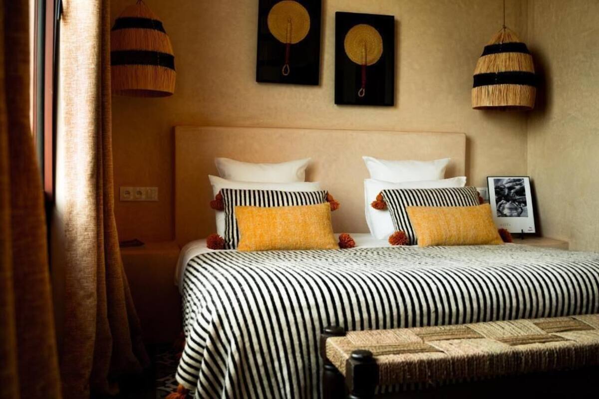 Una cama con ropa de cama a rayas, dos lámparas fijadas a la pared y un cuadro enmarcado.