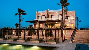 Un edificio moderno con piscina, mobiliario de exterior y palmeras.