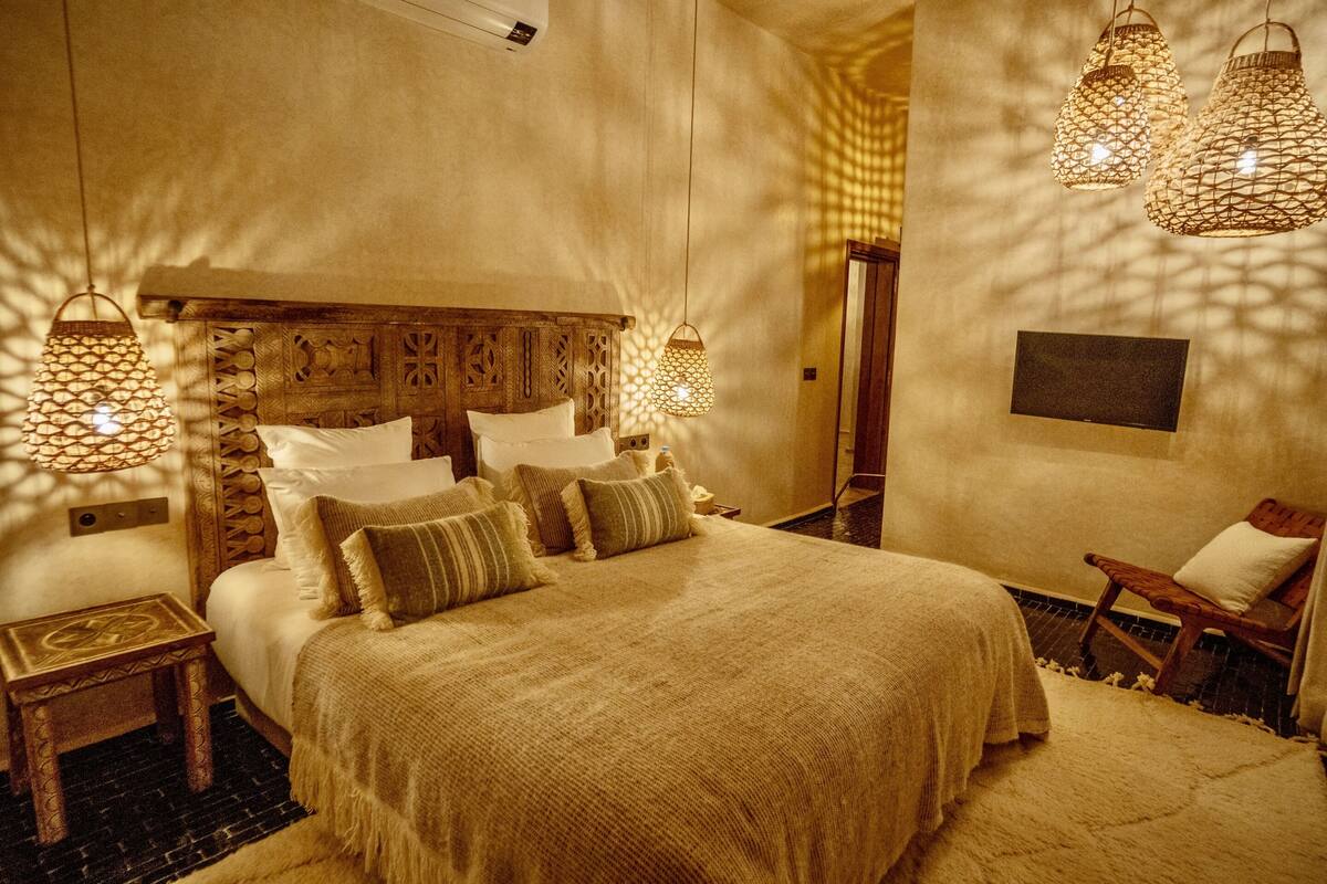 Un dormitorio con una cama grande, mesitas de noche, una silla e iluminación colgante.