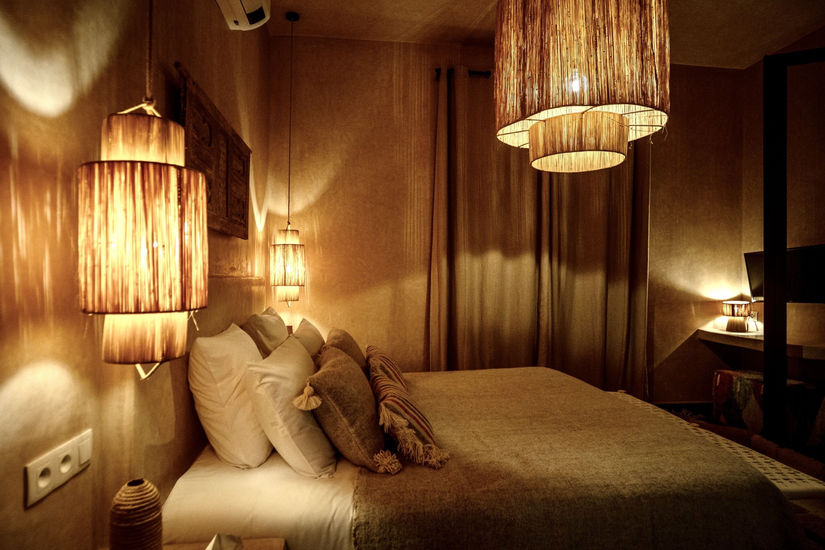 Una habitación de hotel con una cama, dos lámparas de pared, un televisor y un enchufe.