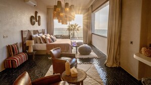 Un dormitorio moderno con una cama grande, un sillón, una mesita y vista al mar.