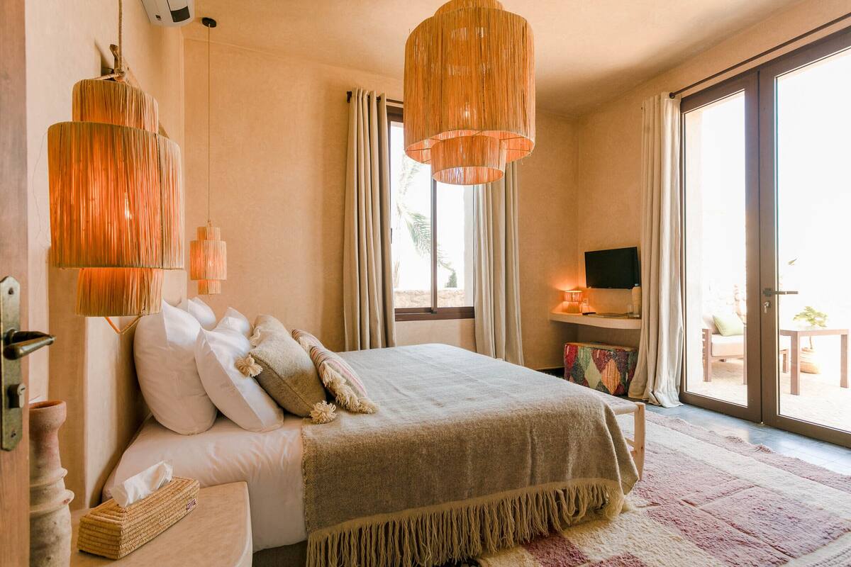 Un dormitorio con cama, lámparas de noche, televisor y vistas al exterior.