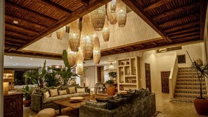 Amplia sala de estar con techo alto, lámparas de luz tejidas, un conjunto de sofás y una escalera con baldosas estampadas.
