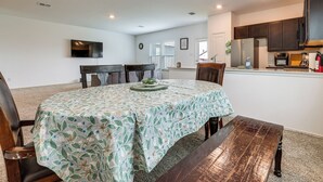 Un comedor con una mesa dispuesta para cuatro personas, una cocina al fondo y un reloj en la pared.