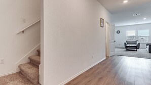 Un pasillo con una escalera alfombrada, una puerta que da a otra habitación y vistas de una sala de estar con un sofá y una ventana.