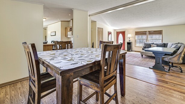 Un coin repas avec une table et des chaises en bois, une cuisine à l’arrière-plan et un salon avec un canapé et une lampe.