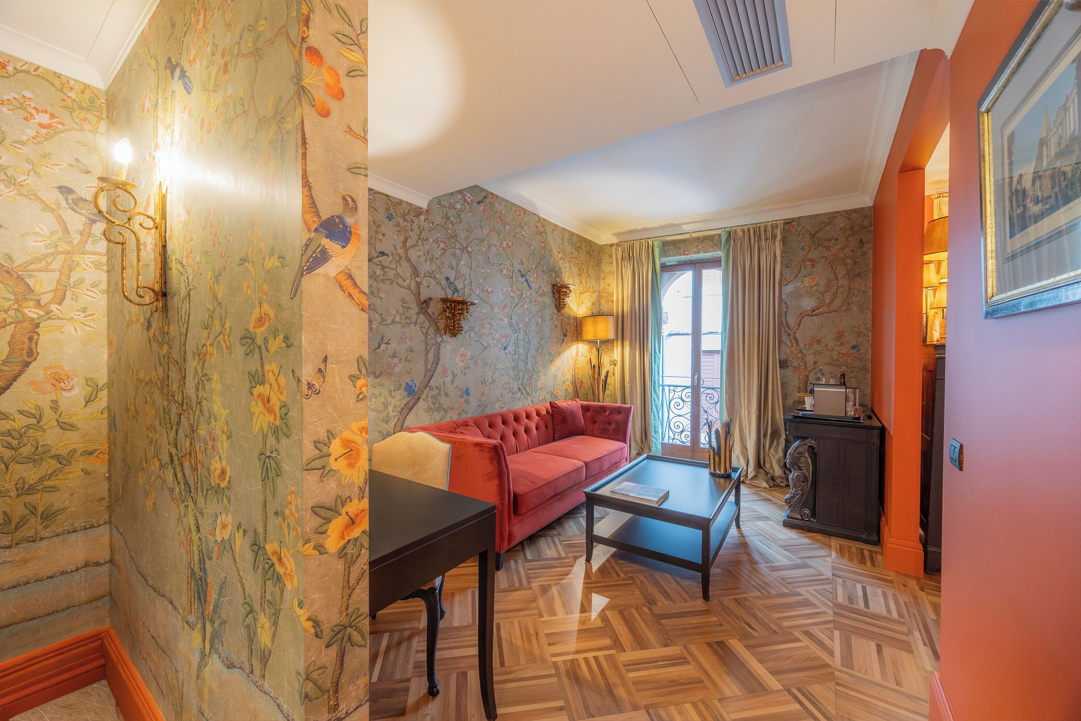 A room with a red sofa, a small table, and a patterned wallpaper.