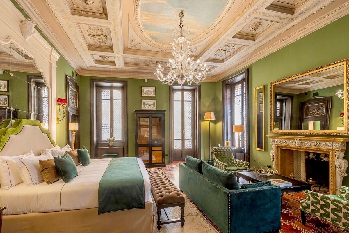 Una habitación con cama, sofá, chimenea y un espejo grande.