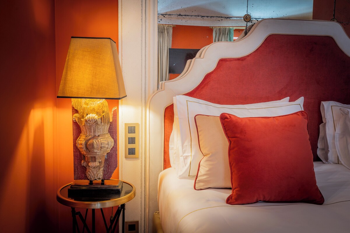 A bed with white and red bedding, a lamp on a side table, and a wall with a textured pattern.