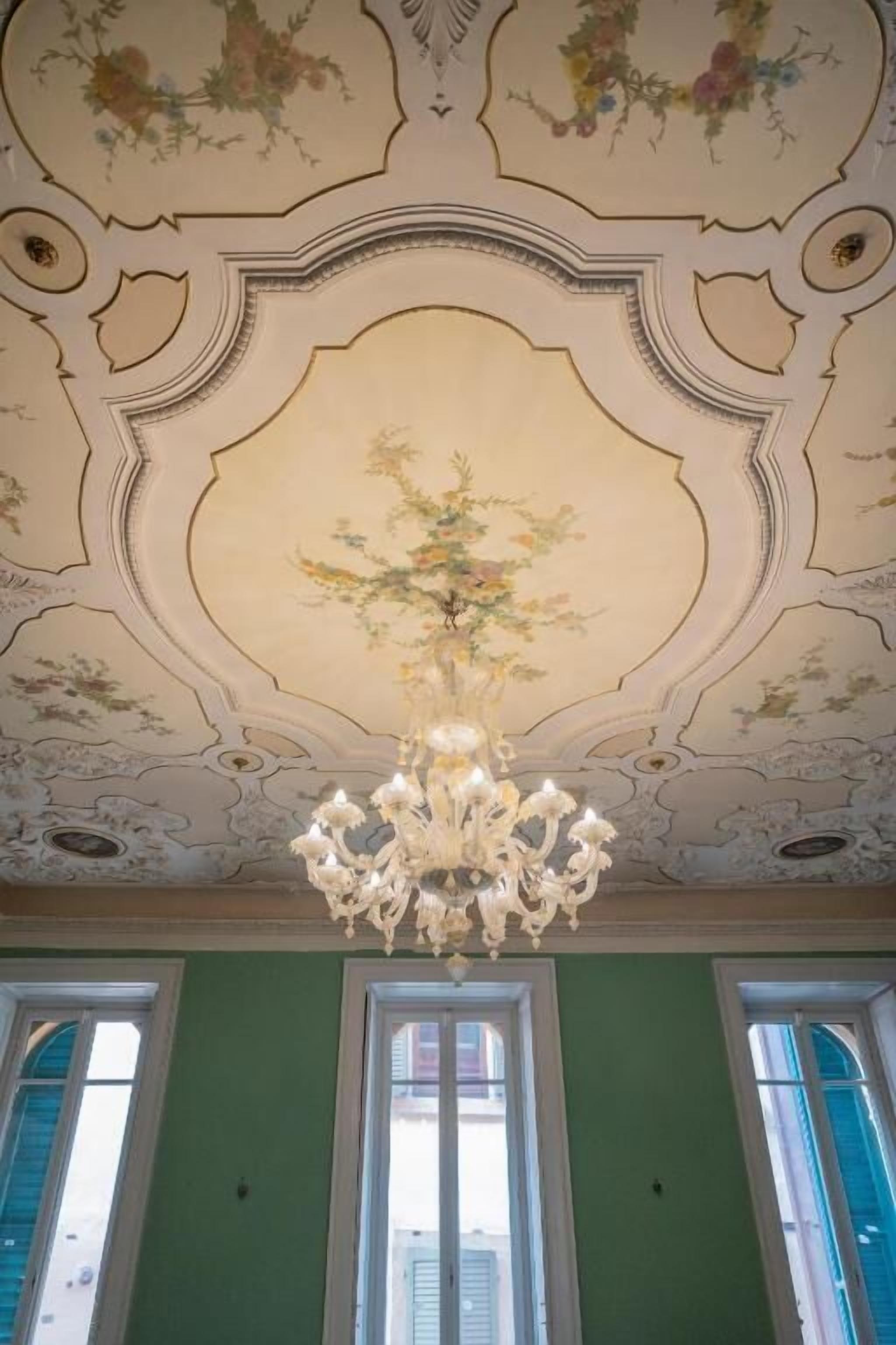A room with a decorative ceiling, a chandelier, and large windows.